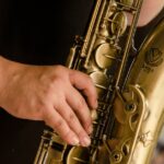 A detailed view of a musician's hand playing a gold saxophone outdoors.