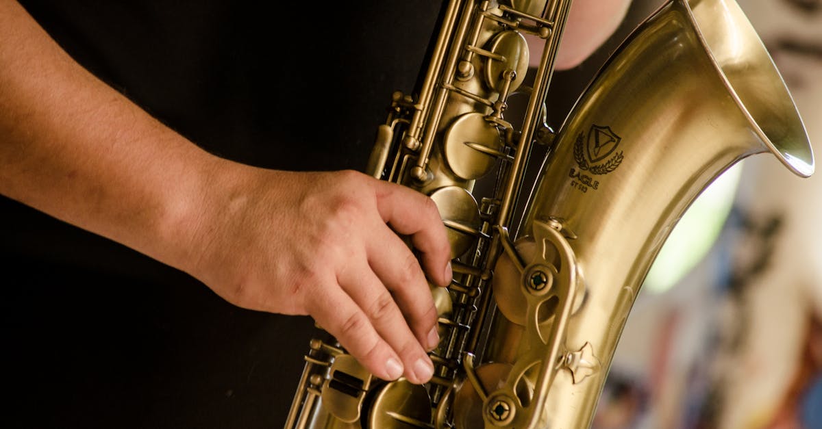 A detailed view of a musician's hand playing a gold saxophone outdoors.