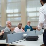 Senior adults attend a computer class, led by an instructor, in a classroom setting.